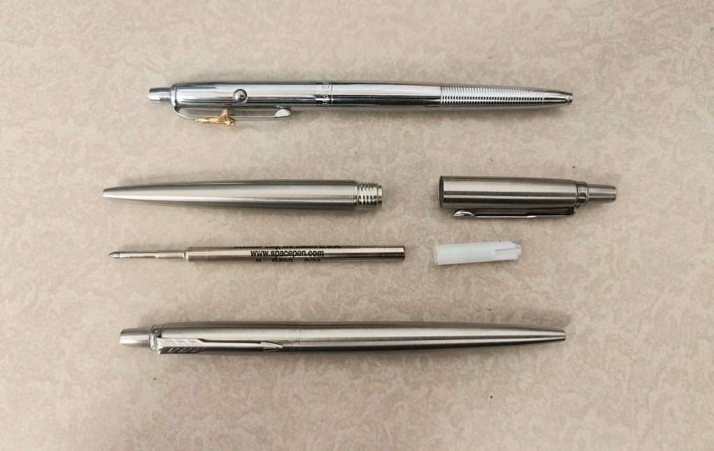 A Fisher Space Pen refill with its plastic adapter next to a Parker Jotter pen
